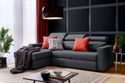 Grijze hoekbank met rode en gedessineerde kussens, versierd met een deken, in een moderne woonkamer met planten en een salontafel, zijaanzicht.
