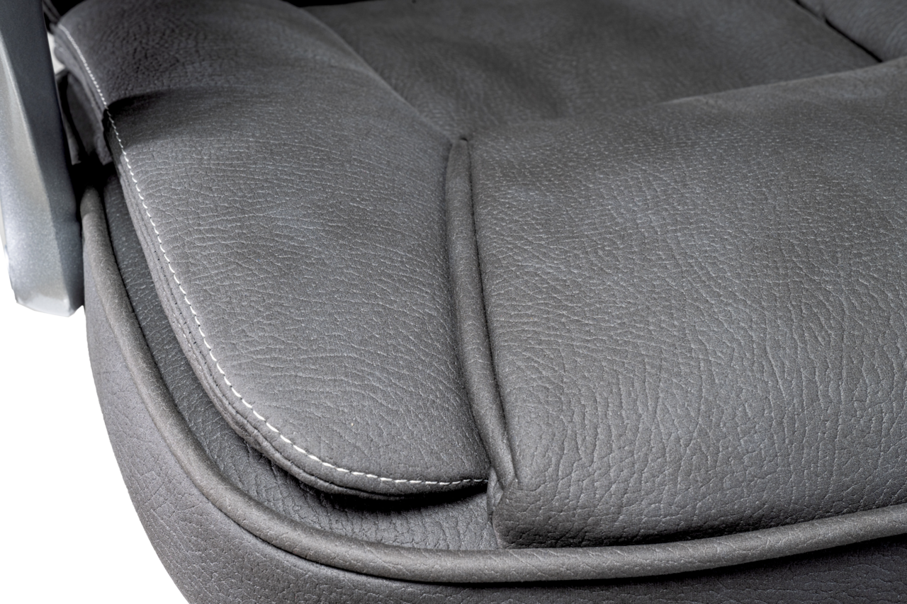 Nahaufnahme der Sitzfläche eines Chefsessels aus grauem Leder mit sichtbaren Nähten, seitliche Perspektive.