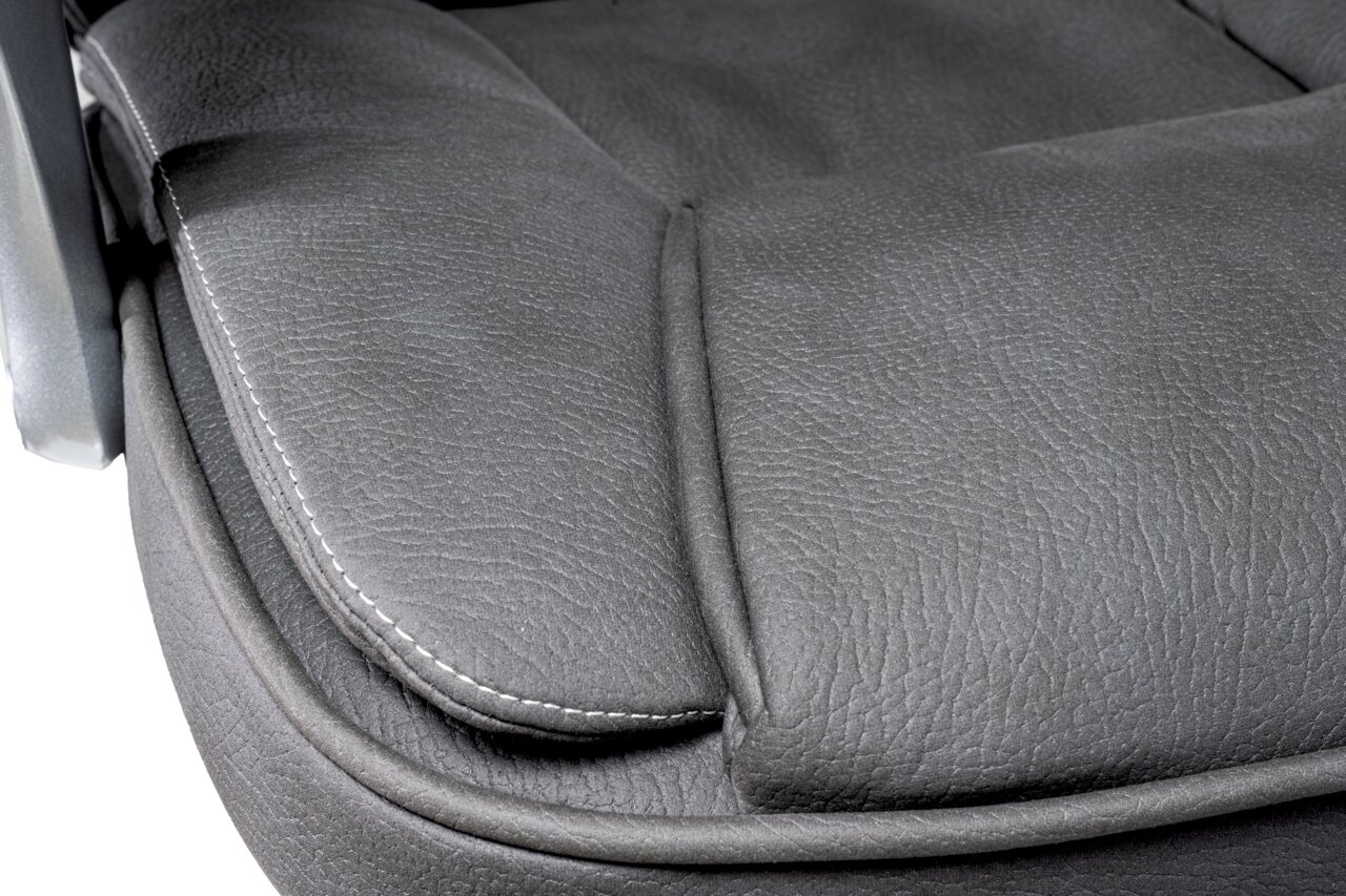 Nahaufnahme der Sitzfläche eines Chefsessels aus grauem Leder mit sichtbaren Nähten, seitliche Perspektive.